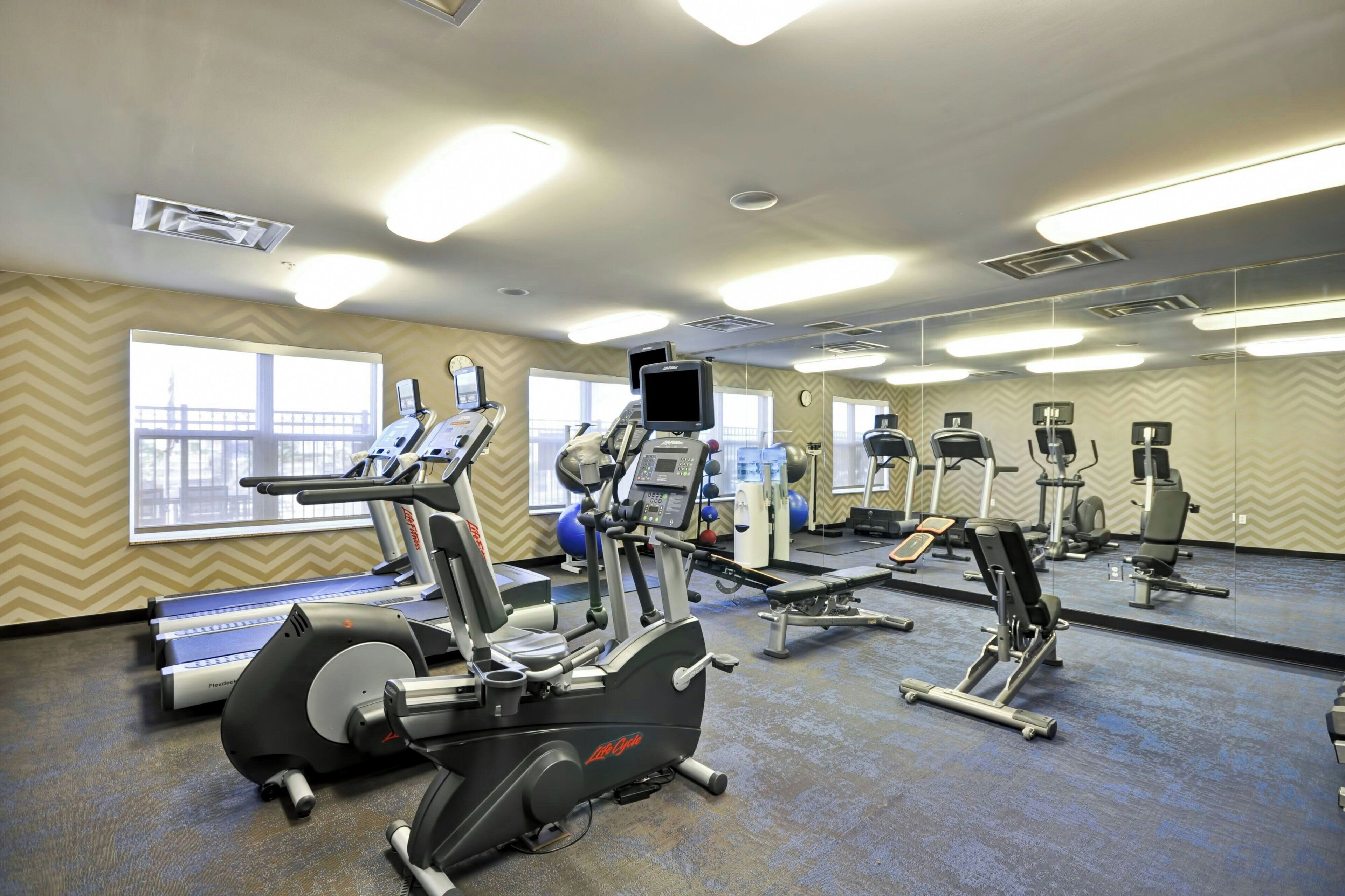 A gym with cardio machines, mirrors, and windows with a view.