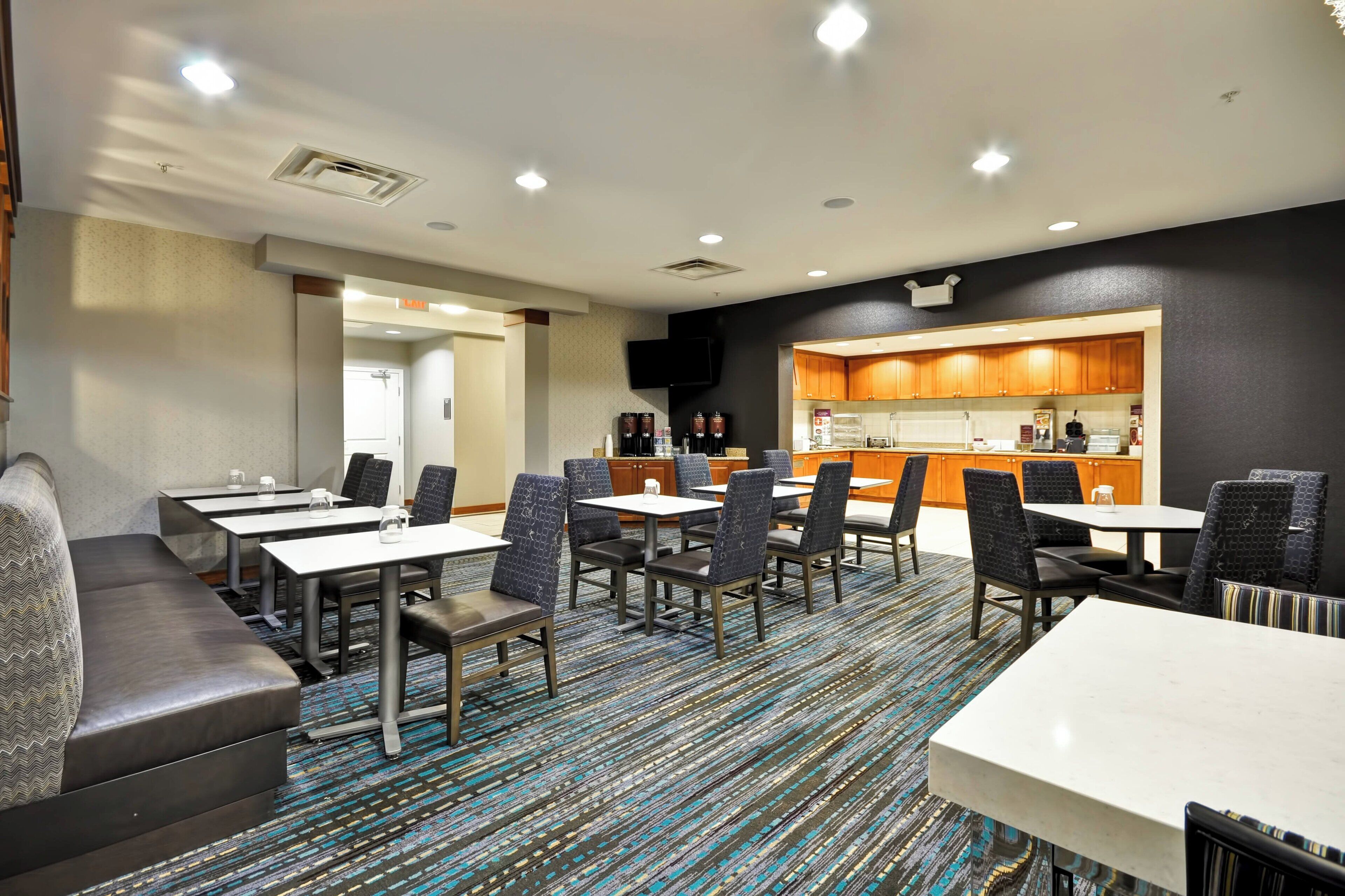Habitación de hotel con comedor, kitchenette y zona de estar con sofá y mesas.