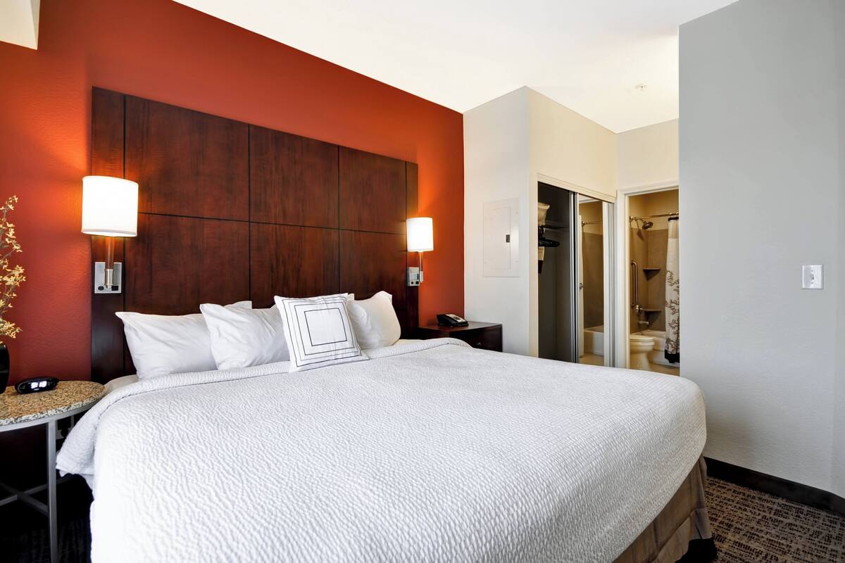 Ein Hotelzimmer mit einem großen Bett, zwei Nachttischlampen, einem Nachttisch und Blick ins Bad.