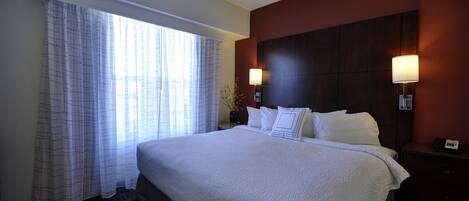 A hotel room with a large bed, two bedside lamps, a window with curtains, and a dark-colored headboard.