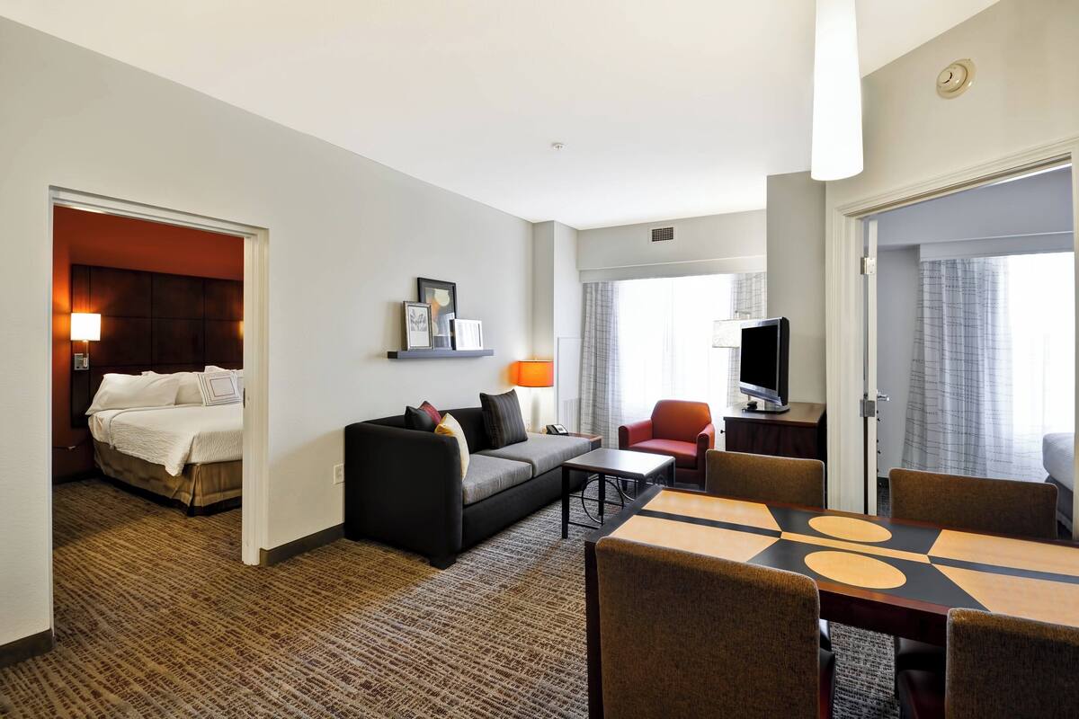 Ein Hotelzimmer mit einem Bett, einer Couch, einem Fernseher, einem Esstisch und einem TV-Schrank.