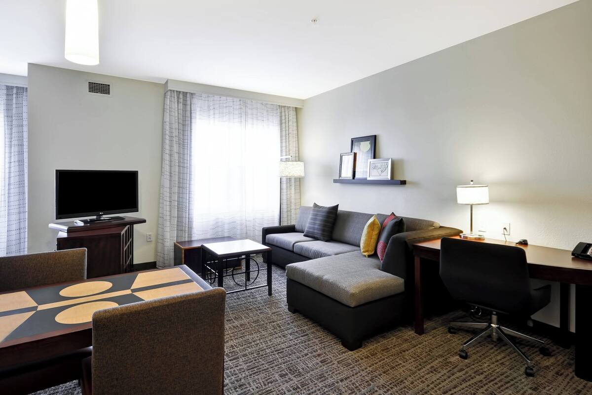 Ein Hotelzimmer mit Flachbildfernseher, einer Sitzecke, einem Schreibtisch, einem Stuhl und einem Esstisch.