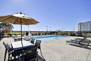 A poolside area with lounge chairs, a table, and an umbrella.