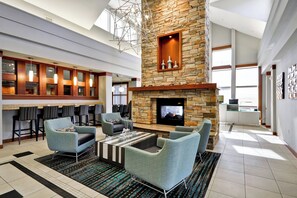 A spacious lobby with a stone fireplace, comfortable seating, a bar area, and large windows allowing natural light.