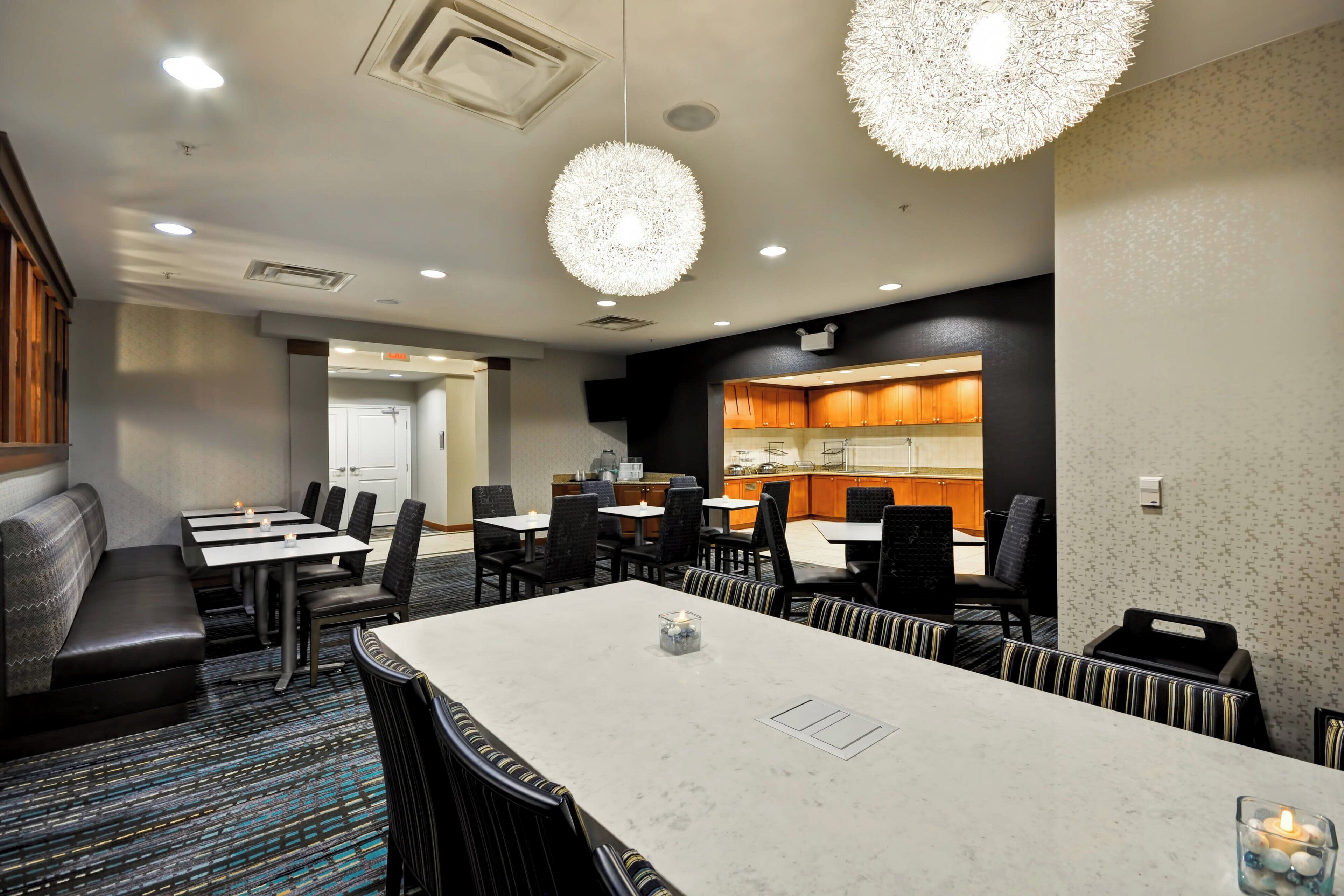 A conference room with a large table, chairs, and a seating area. There are two pendant lights hanging from the ceiling.
