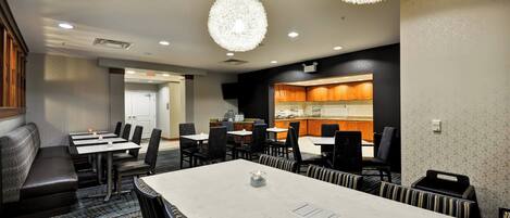 A conference room with a large table, chairs, and a seating area. There are two pendant lights hanging from the ceiling.