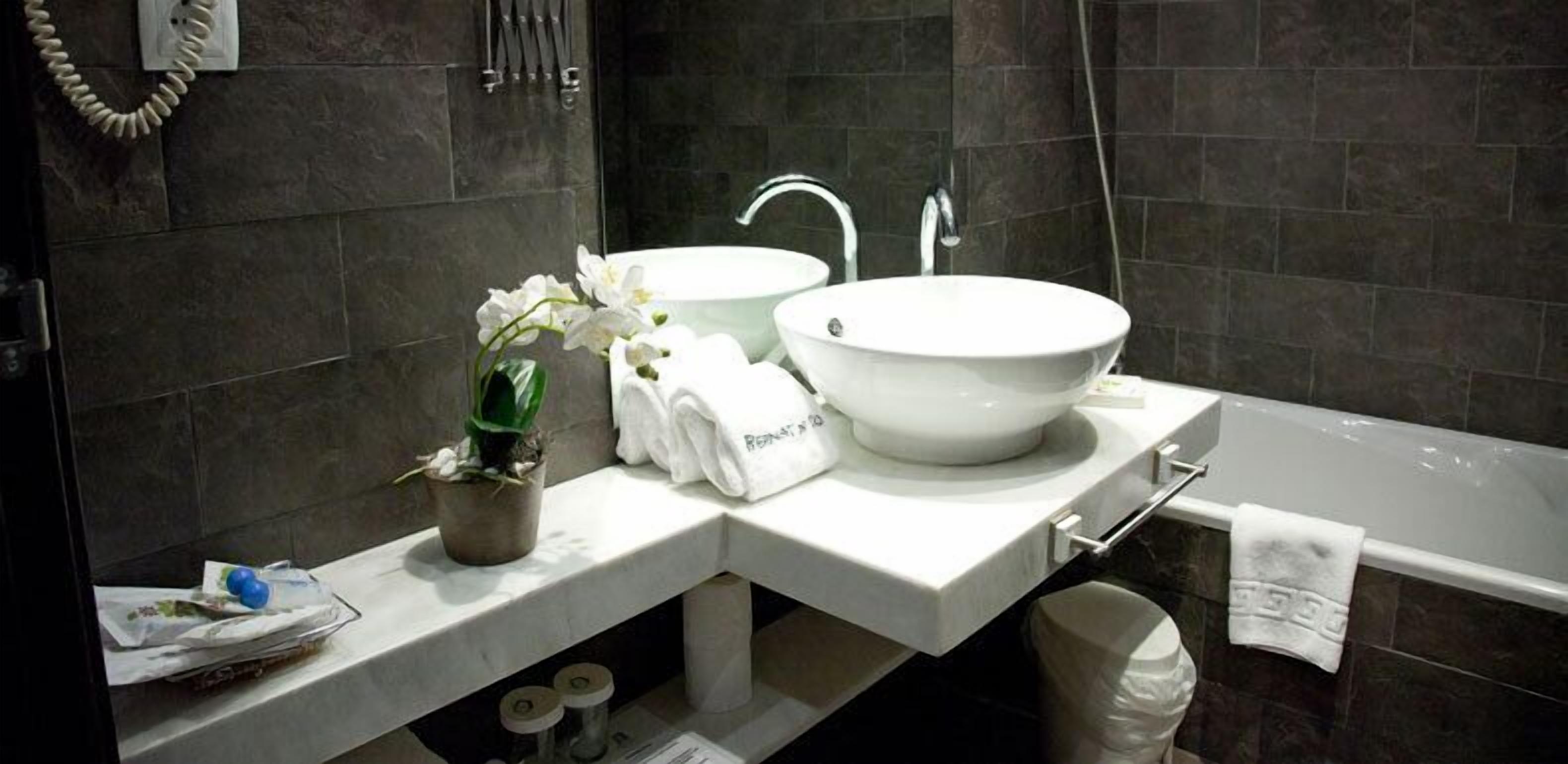 A modern bathroom with two white sinks, a large bathtub, a towel rack, and a potted plant.