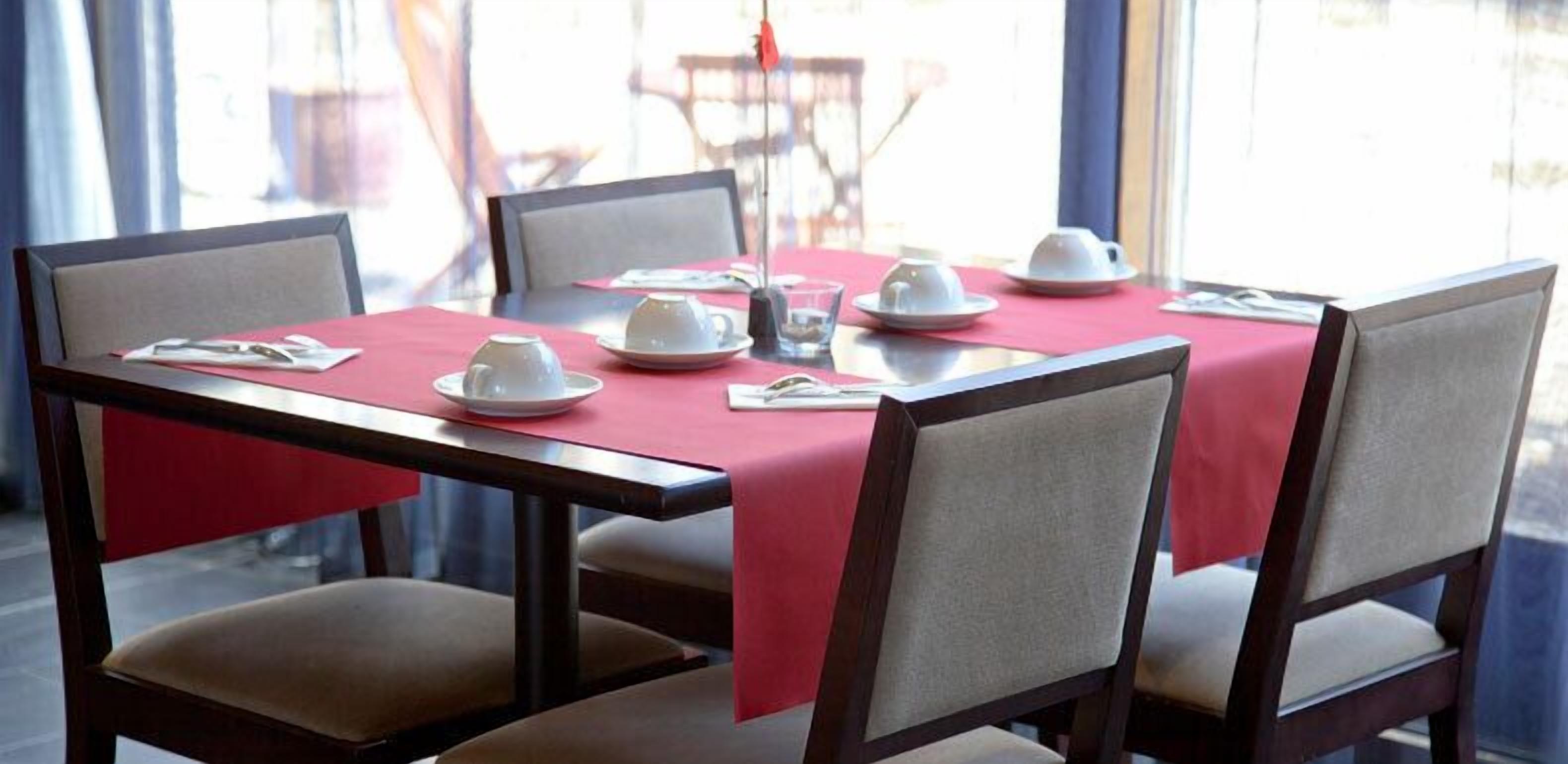 A dining table set with white teacups and saucers, a glass, and a menu.
