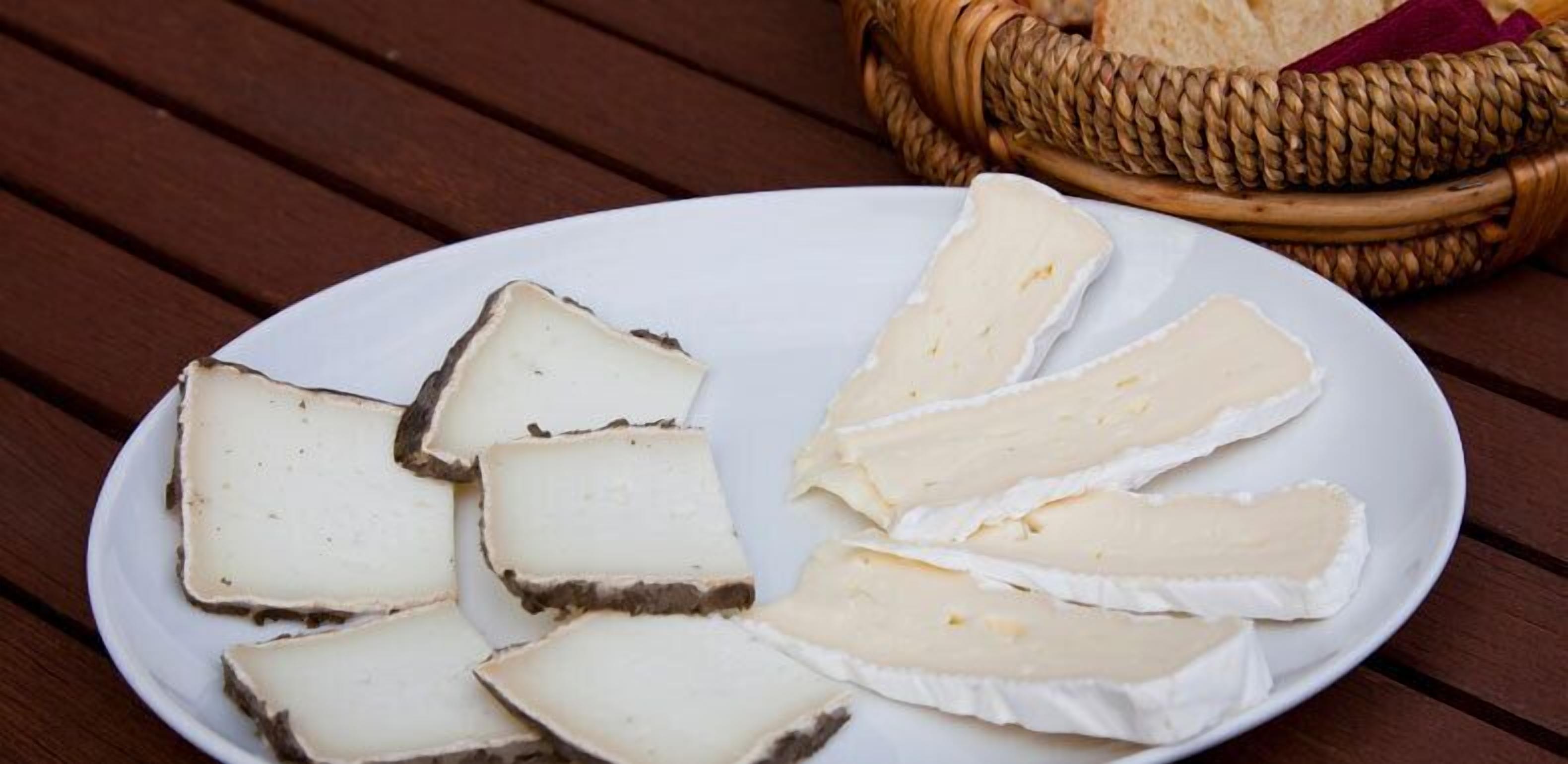 Un plato de rebanadas de queso sobre una mesa de madera, con una cesta de pan al fondo.