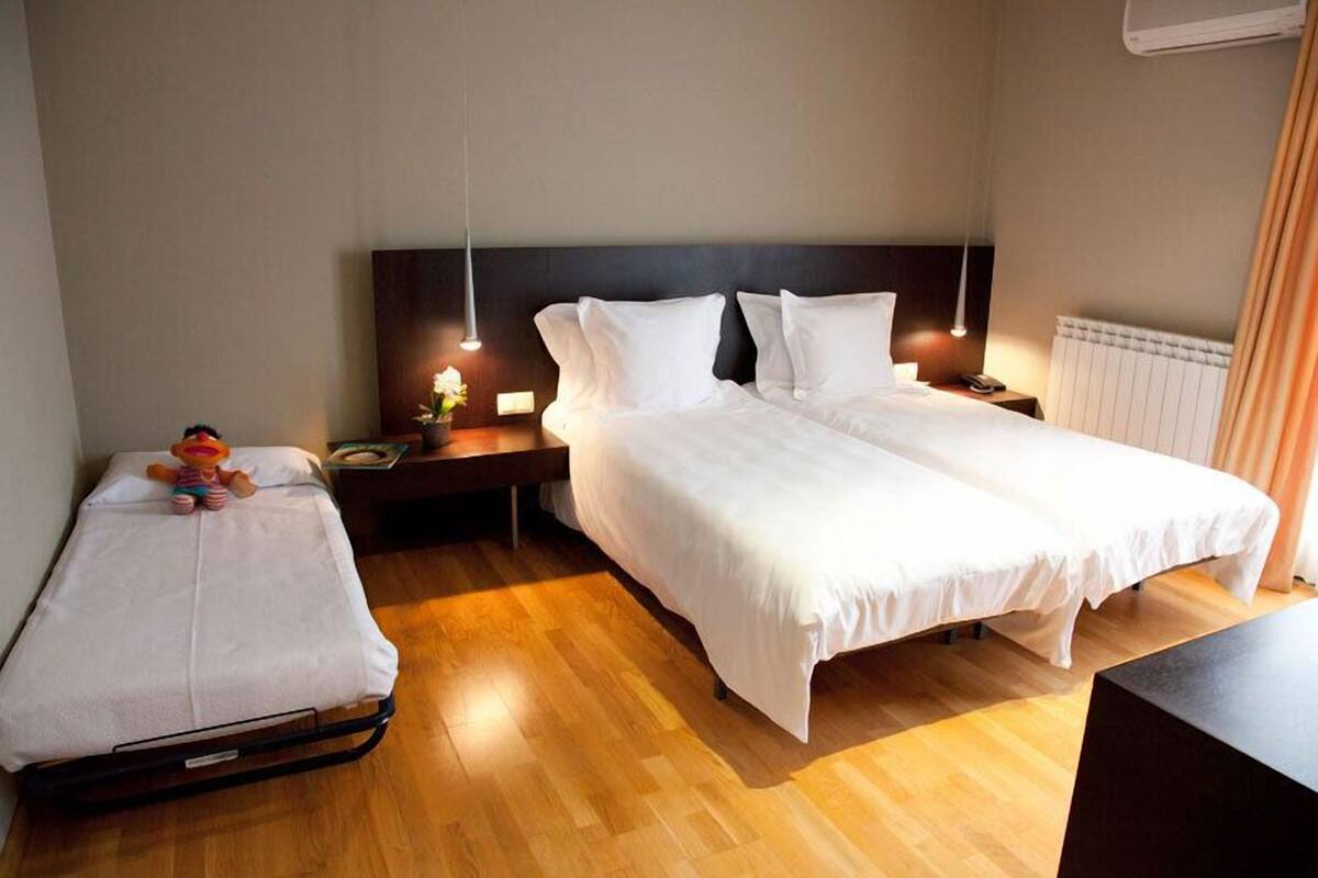 Une chambre d’hôtel avec deux lits, un plancher en bois, une table de chevet avec une lampe et une petite table avec un jouet.