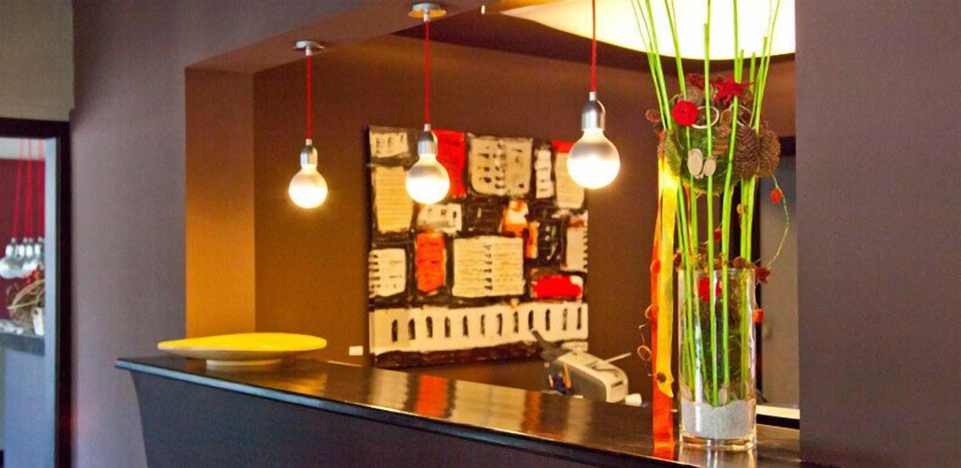 Una cocina moderna con encimera negra, luces colgantes y una pared decorativa con una mezcla de patrones y colores.