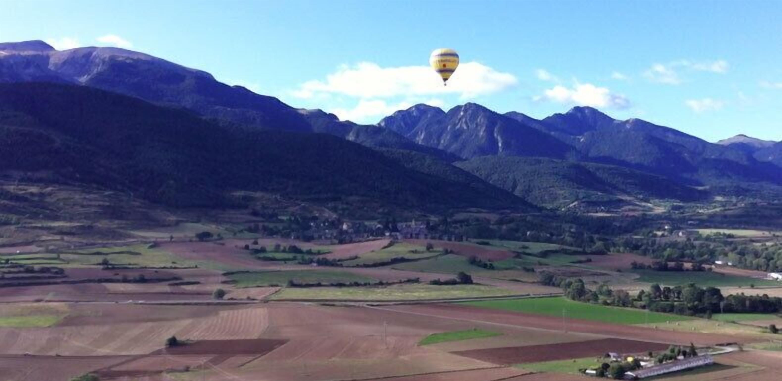 Eine Heißluftballon über einem Tal mit Bergen im Hintergrund.