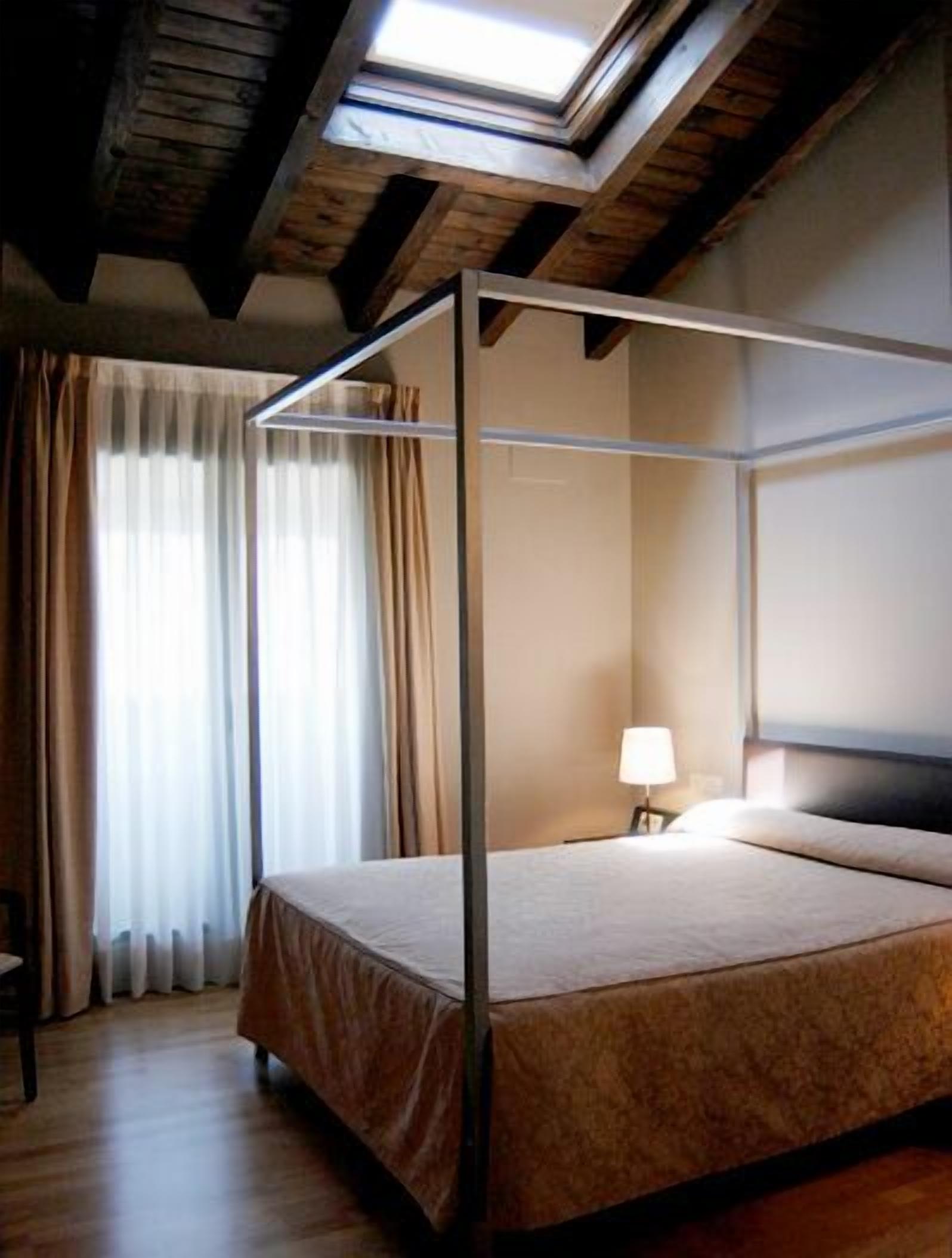Una cama con dosel en una habitación con techo inclinado y vigas de madera.