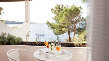 Una mesa con bebidas y un jarrón de flores en una terraza con vista al mar.