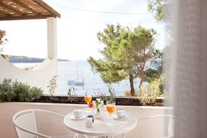 A table with drinks and a vase of flowers on a terrace with a view of the sea.