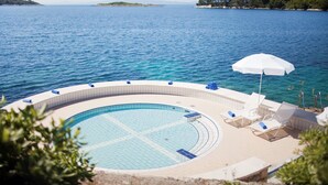 A circular pool with lounge chairs and an umbrella, surrounded by a poolside area with a view of the sea. - Hotel Odisej (Mljet)