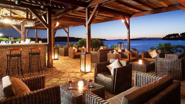 An outdoor seating area with wicker furniture, a bar, and a view of the water. - Hotel Odisej (Mljet)