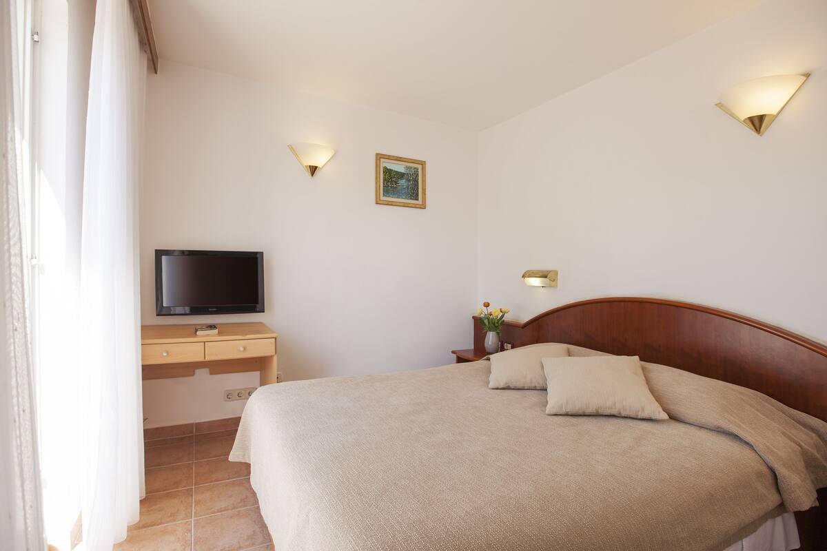 A neatly arranged bedroom with a bed, a TV on a wooden dresser, and two wall-mounted lights.