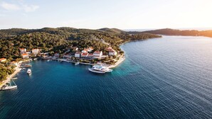 An aerial view of a coastal town with a marina, houses with red roofs, and a clear blue sea. - Hotel Odisej (Mljet)