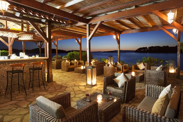 An outdoor patio with wicker furniture, stone flooring, and a bar area with glasses and bottles.