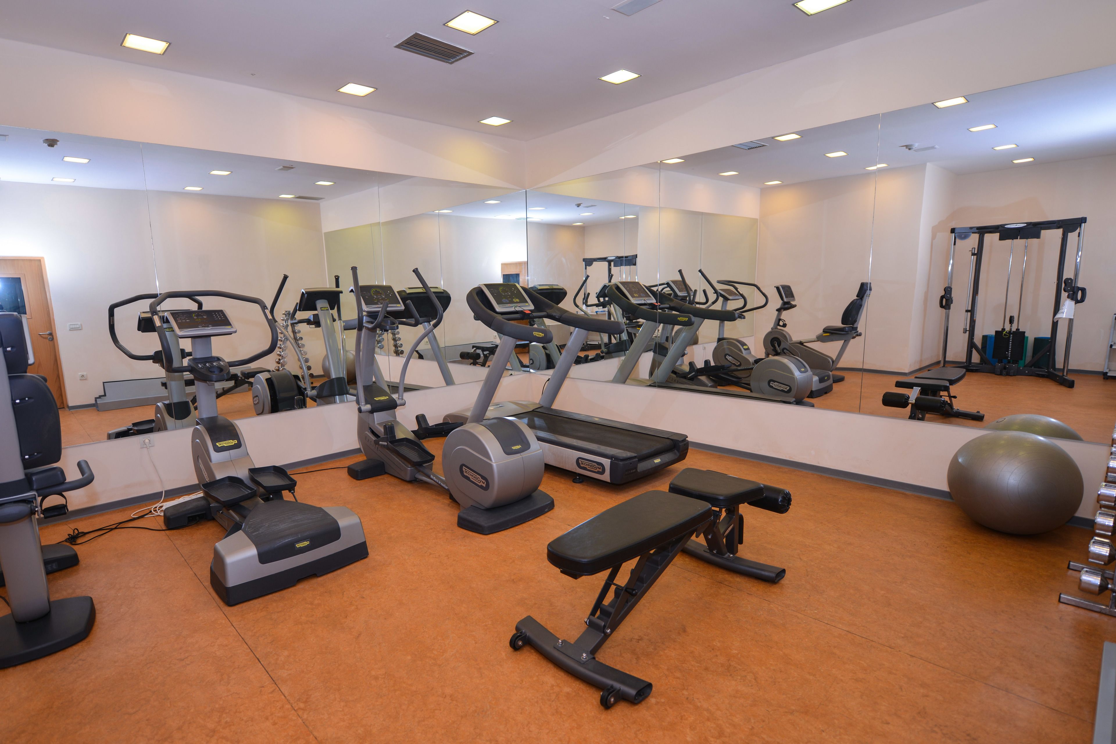 A gym with exercise equipment, a large mirror, and orange flooring.