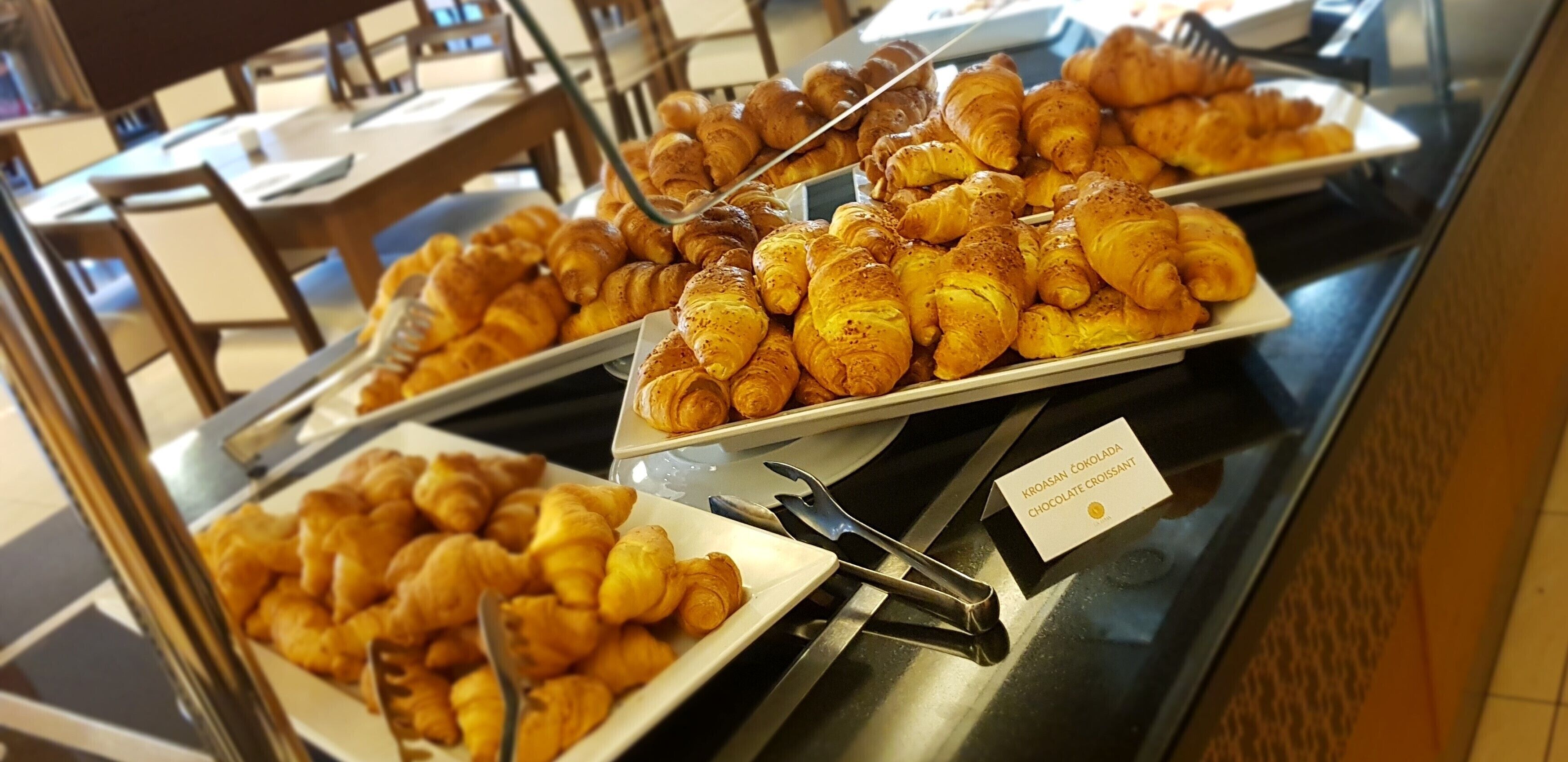 Un bufé con diversos tipos de pasteles, incluyendo croissants y medialunas de chocolate, dispuestos en platos.