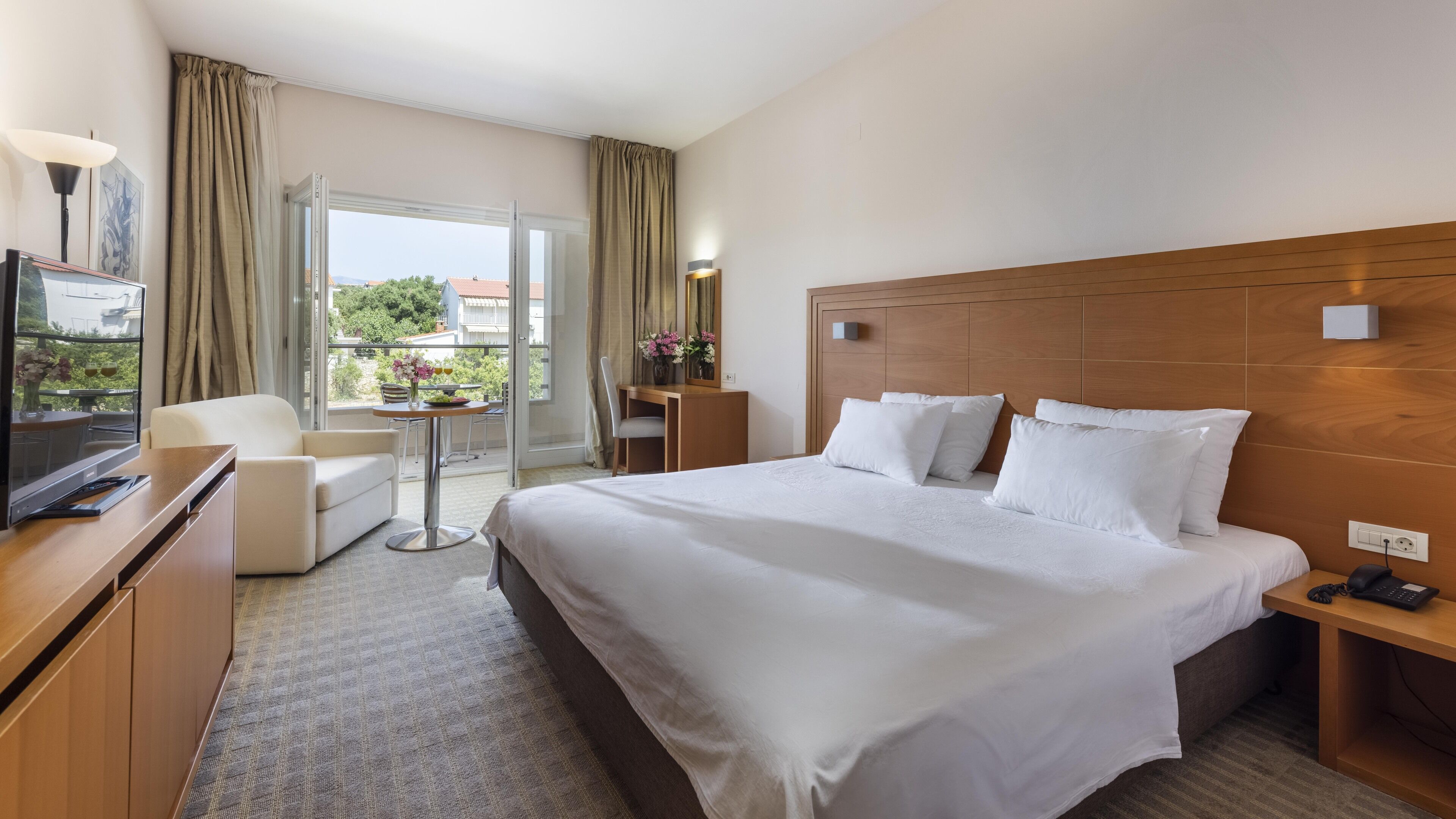 A hotel room with a large bed, a desk, a chair, and a television.