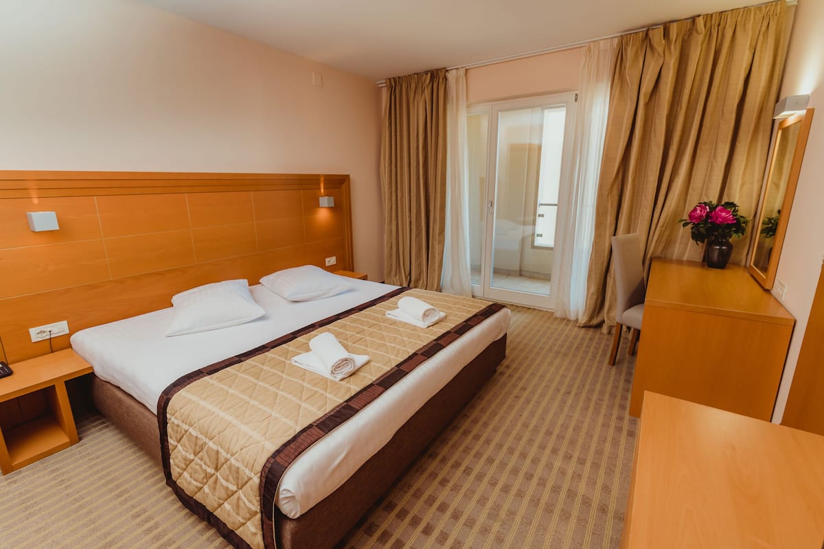 A hotel room with a large bed, a desk, a chair, and a balcony with curtains.