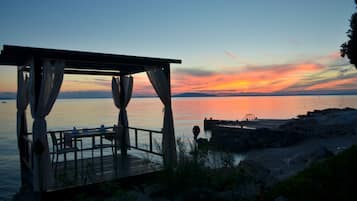 Una terraza de madera con una mesa y sillas, con vista a una masa de agua tranquila durante el atardecer.