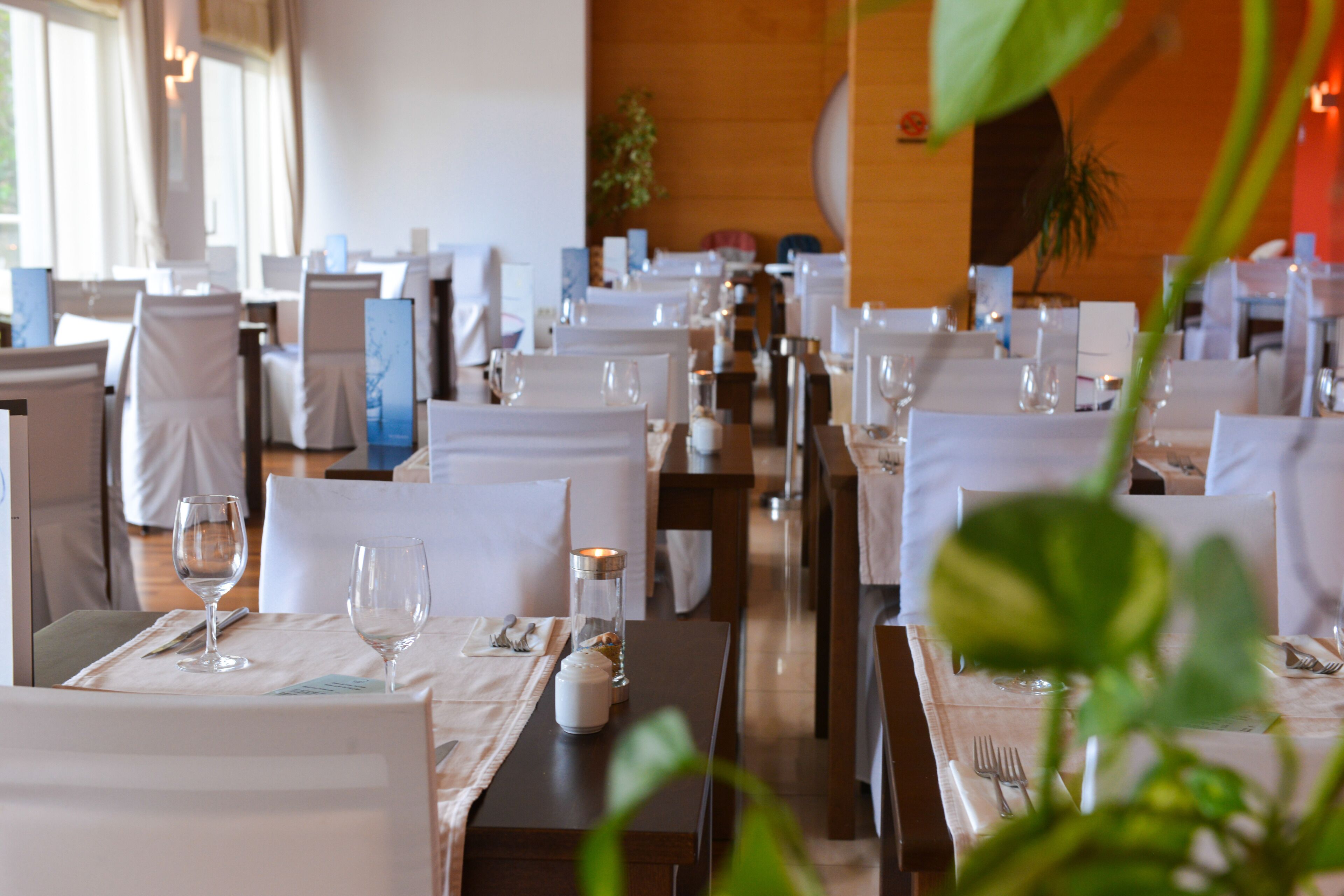 En restaurant med flere borde dækket til spisning, alle med hvide duge, vinglas og bestik.