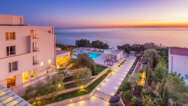 A modern hotel with a swimming pool, landscaped gardens, and a view of the sea at sunset. - Family Hotel La Luna (Novalja)