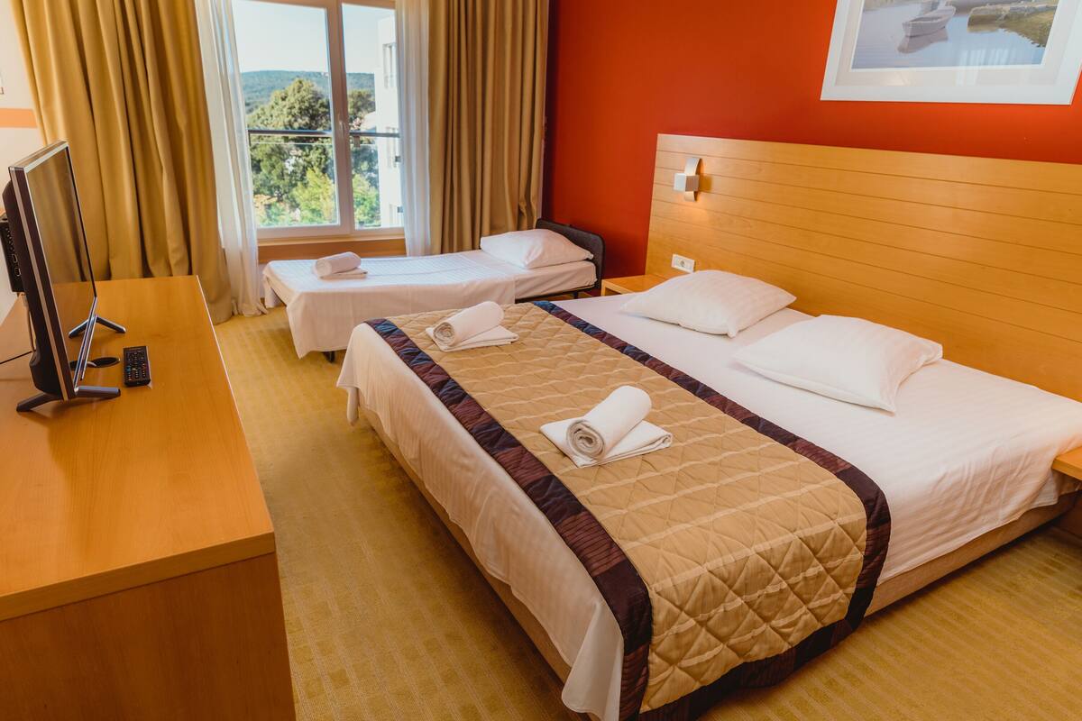 A hotel room with two beds, a desk with a computer and phone, and a window with curtains.