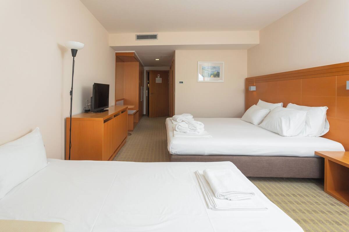 A hotel room with two beds, a TV, a desk, and a lamp.