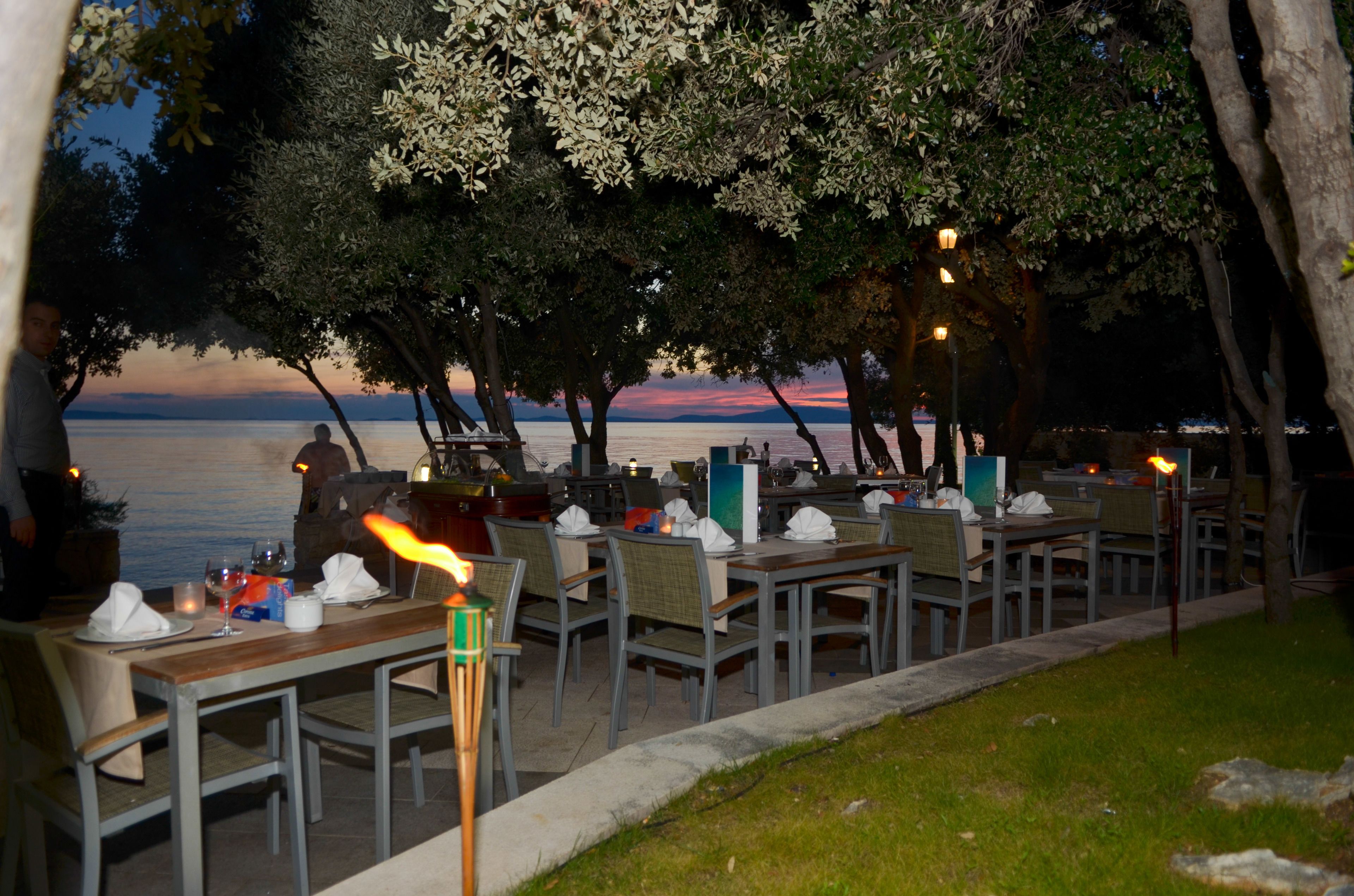 An outdoor dining area with tables and chairs, a view of the water, and trees.