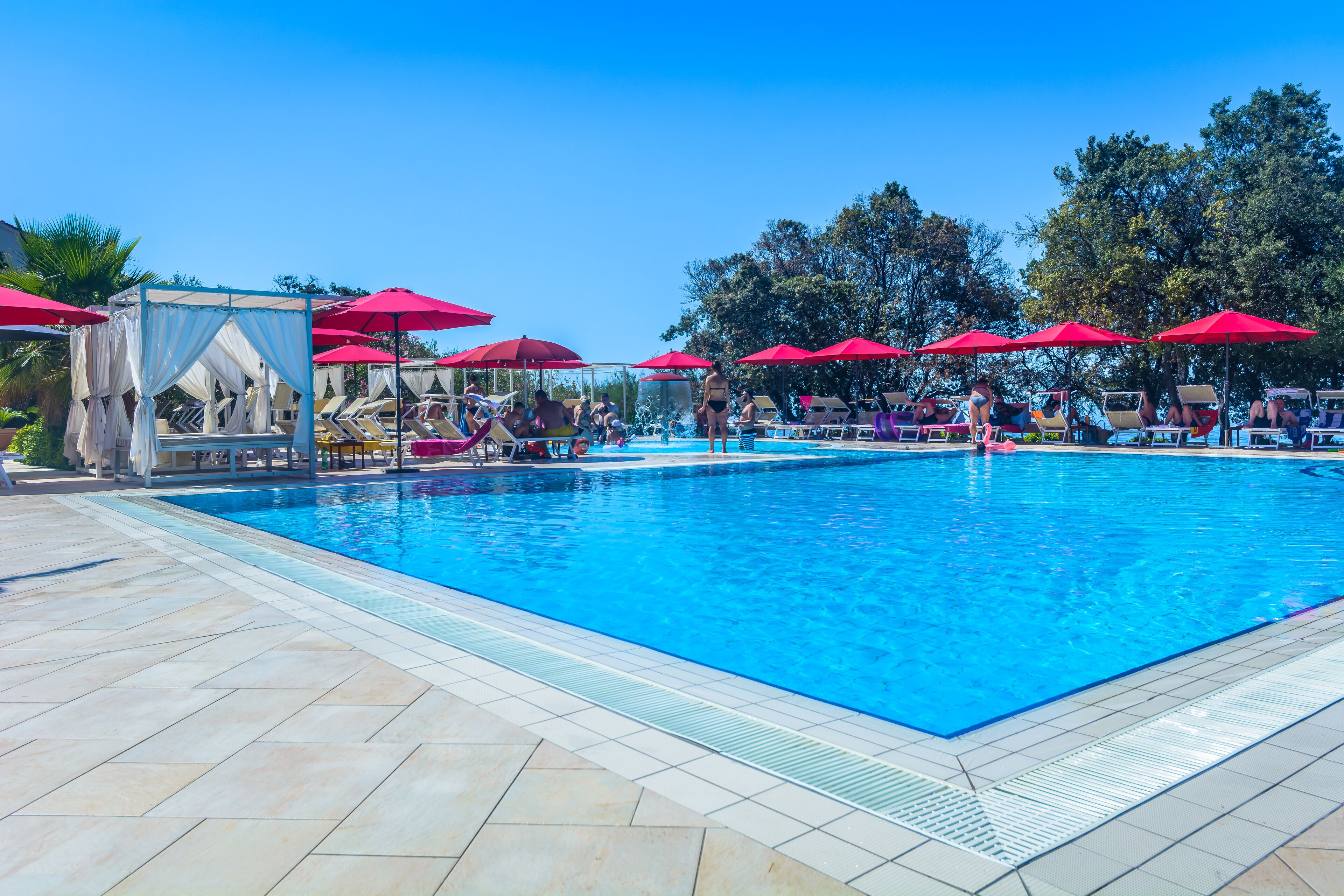 Ein Pool mit roten Sonnenschirmen und Liegestühlen.