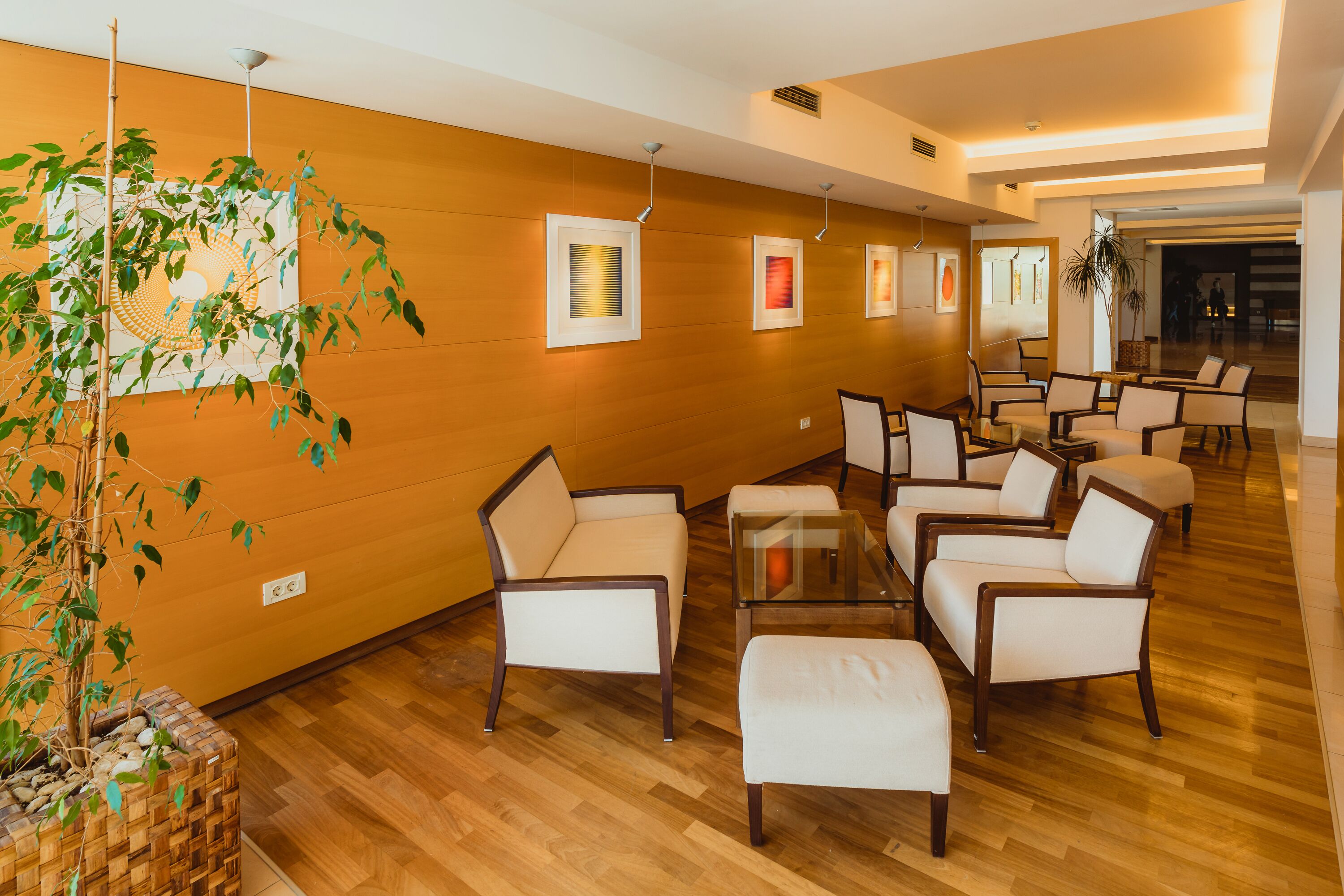 A lobby with wooden flooring, white armchairs, a glass coffee table, and framed artwork on the walls.