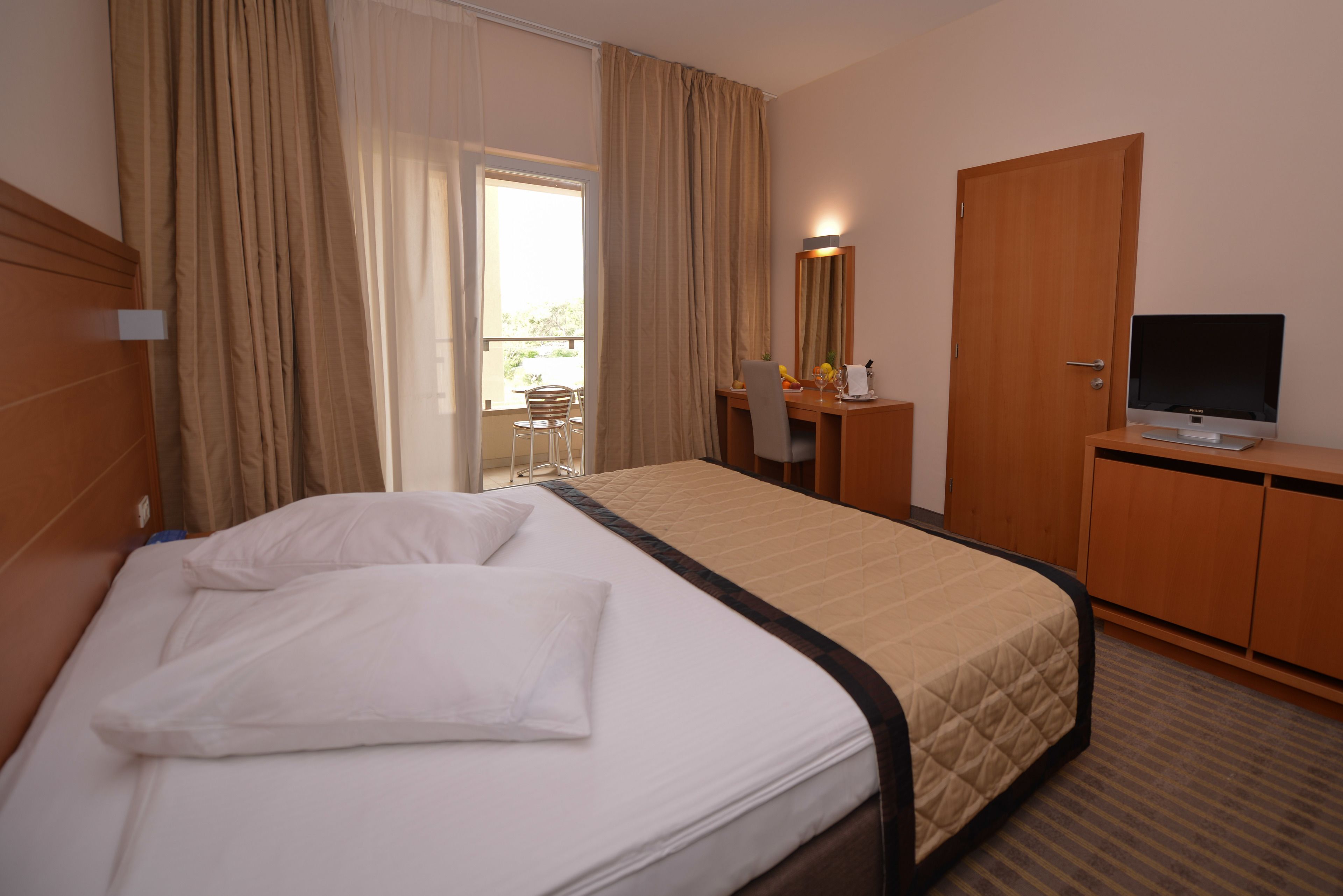 Una habitación de hotel con cama, escritorio, televisión y ventana con cortinas.