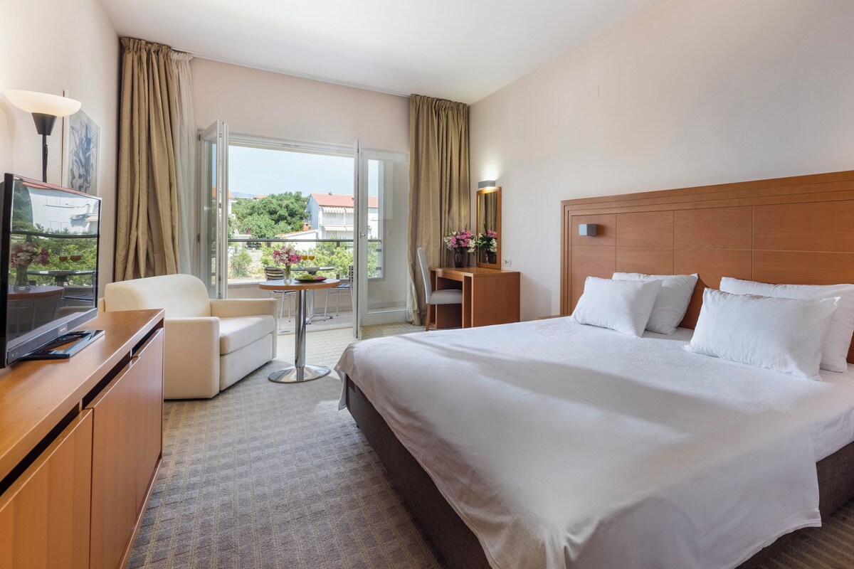 A hotel room with a large bed, a desk, a chair, and a television.