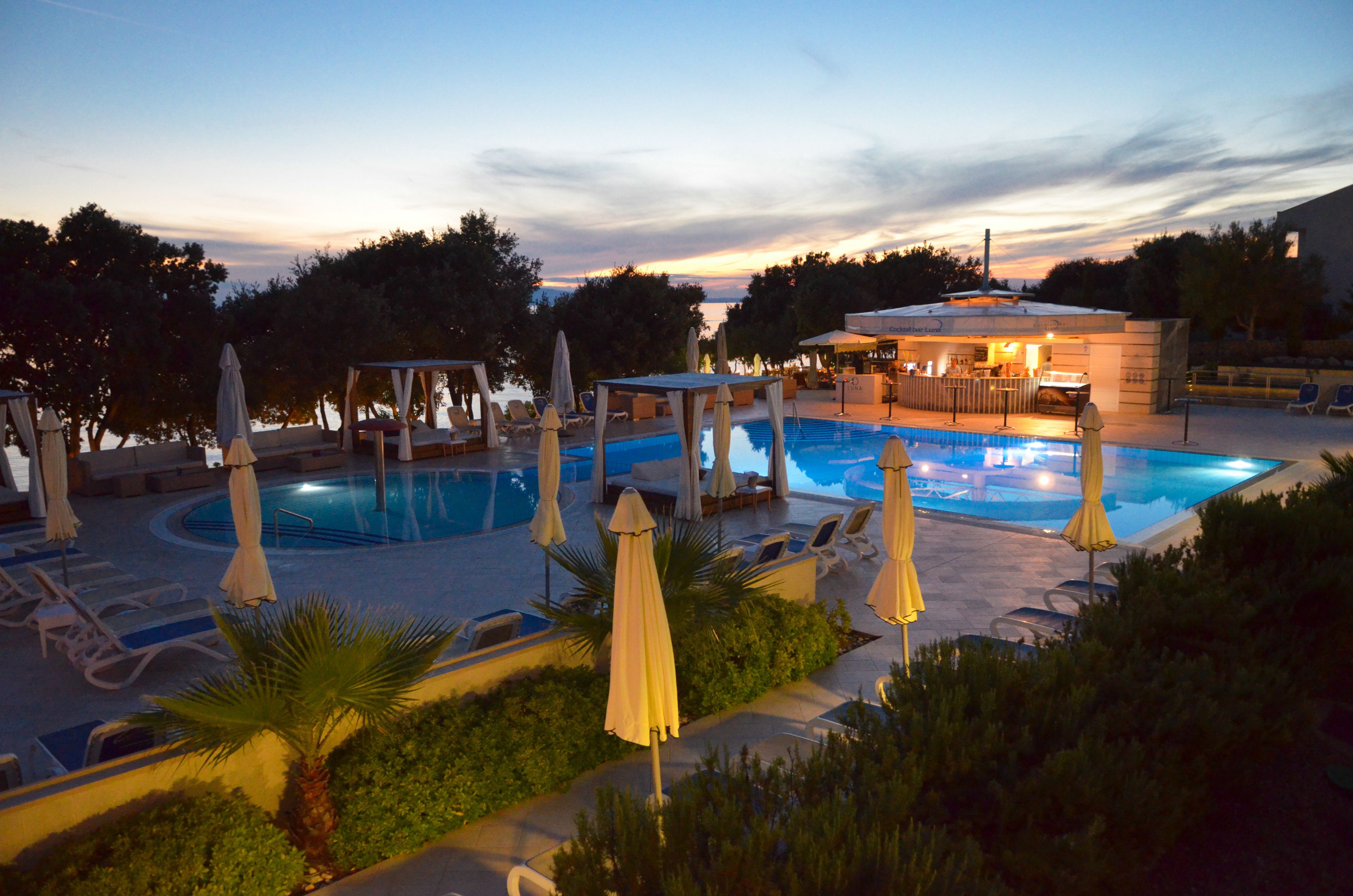 A pool area with lounge chairs and umbrellas, surrounded by greenery.