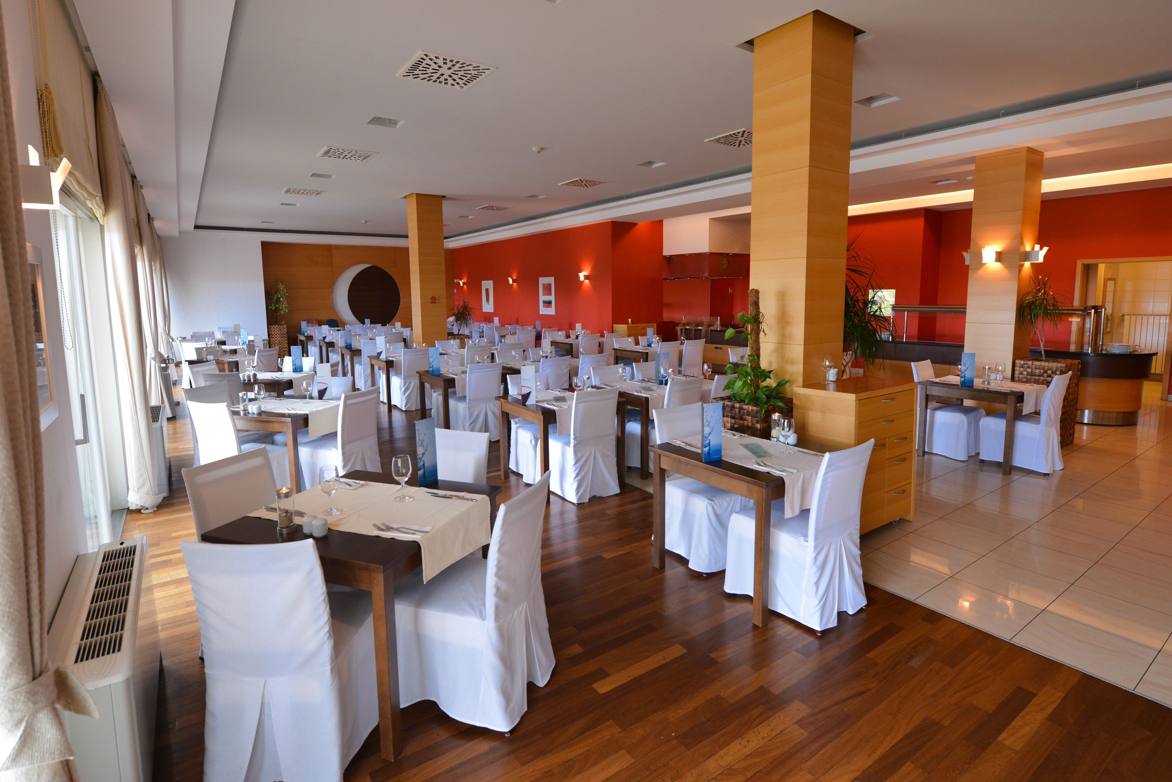 A spacious dining area with multiple tables and chairs, large pillars, and a red accent wall.