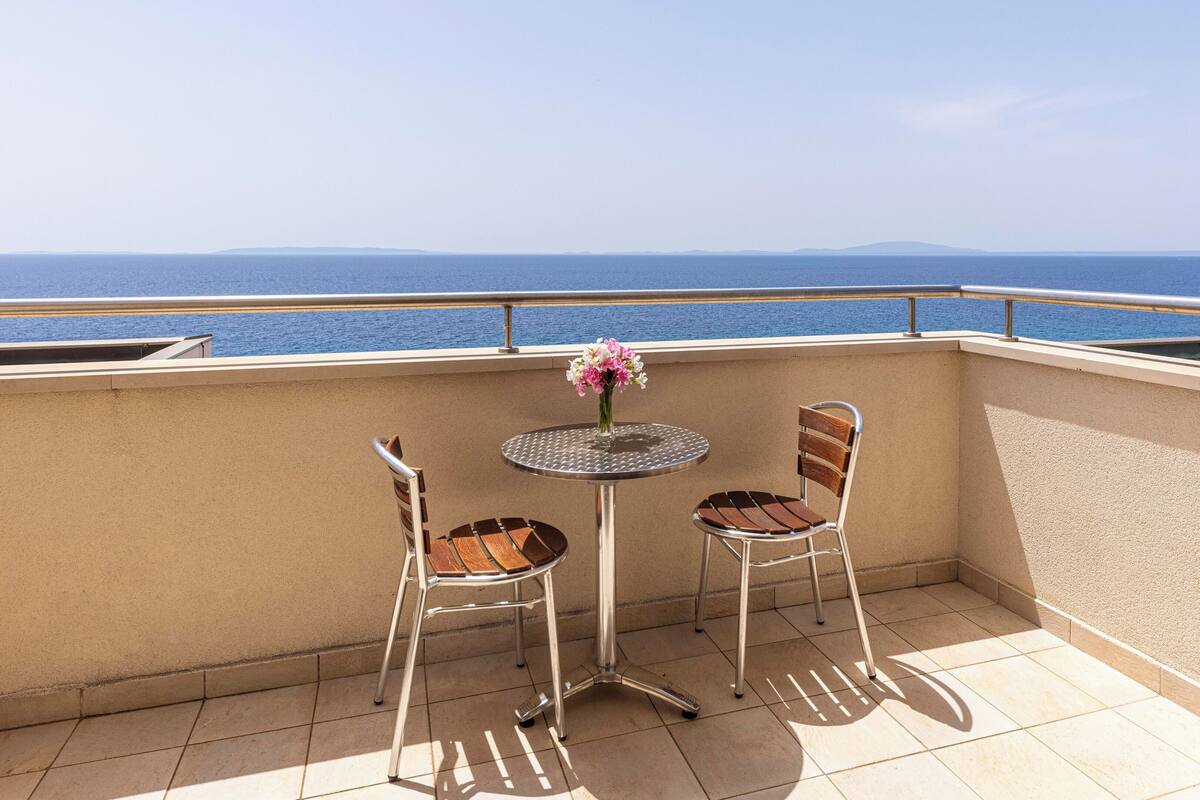A balcony with two chairs and a table, overlooking a body of water.