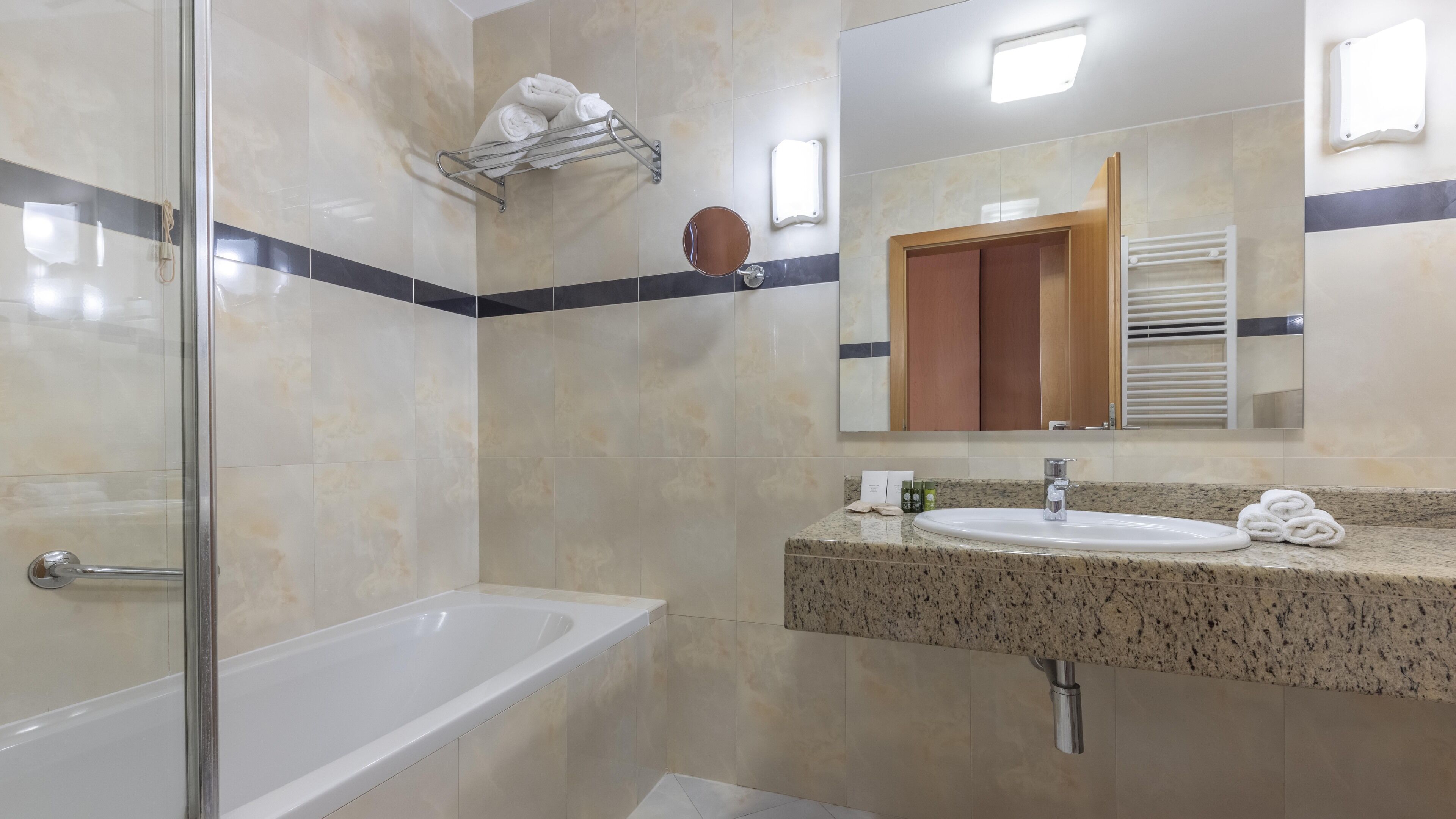 Un bagno moderno con box doccia in vetro, una vasca da bagno bianca, un lavabo con piano in granito e uno specchio grande.