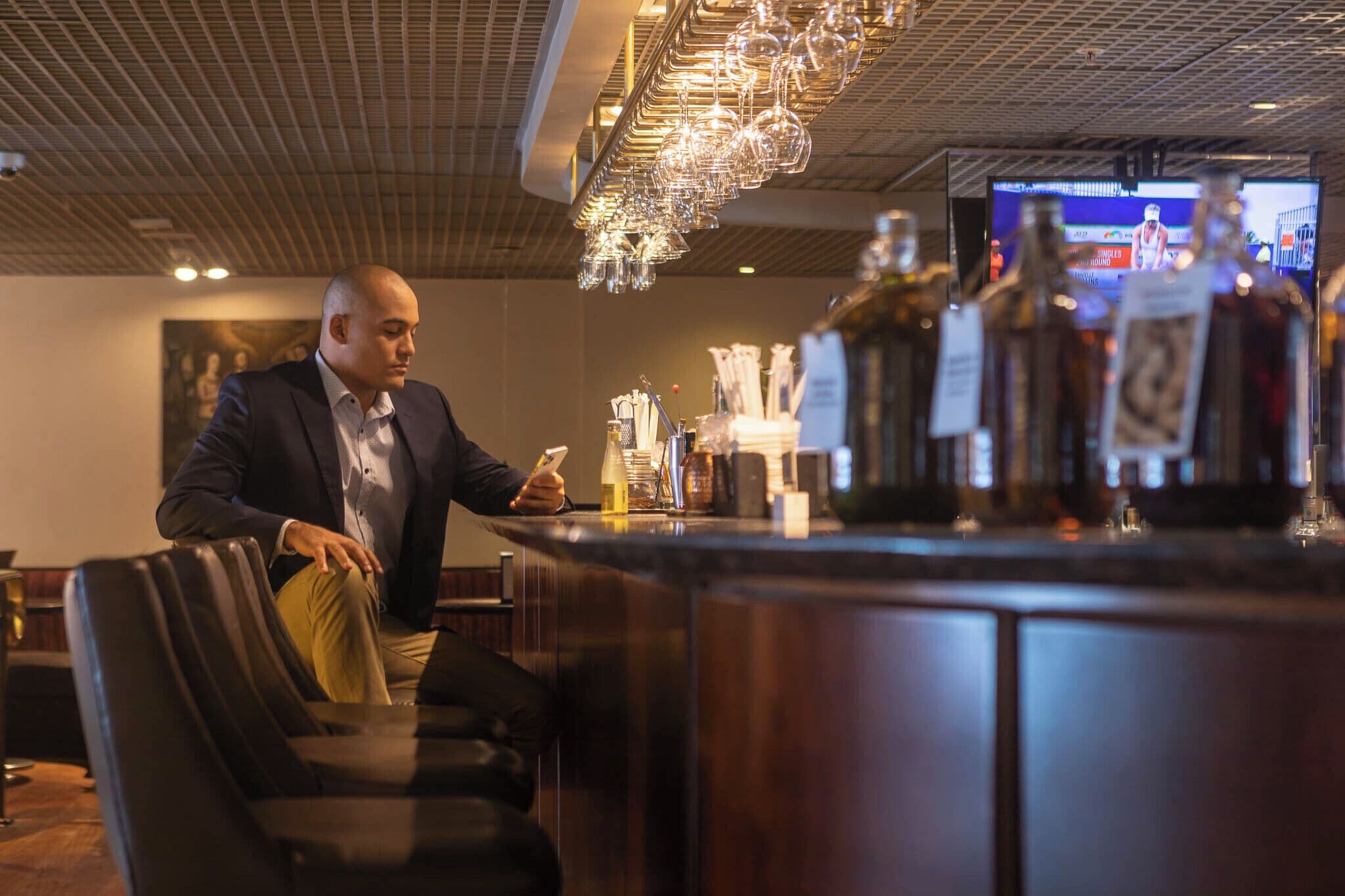 A man seated at a bar with a television screen in the background.