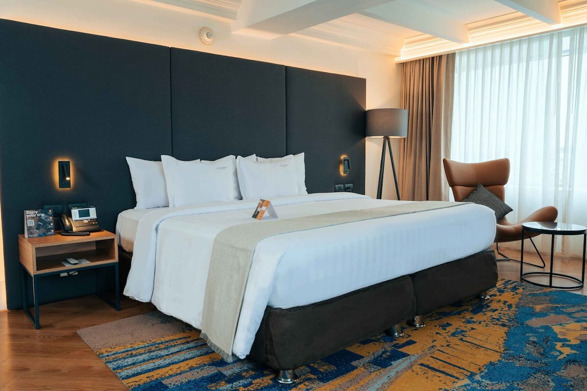 Une chambre d’hôtel avec un grand lit, des tables de chevet, une chaise, une lampe et une vue sur l’extérieur.