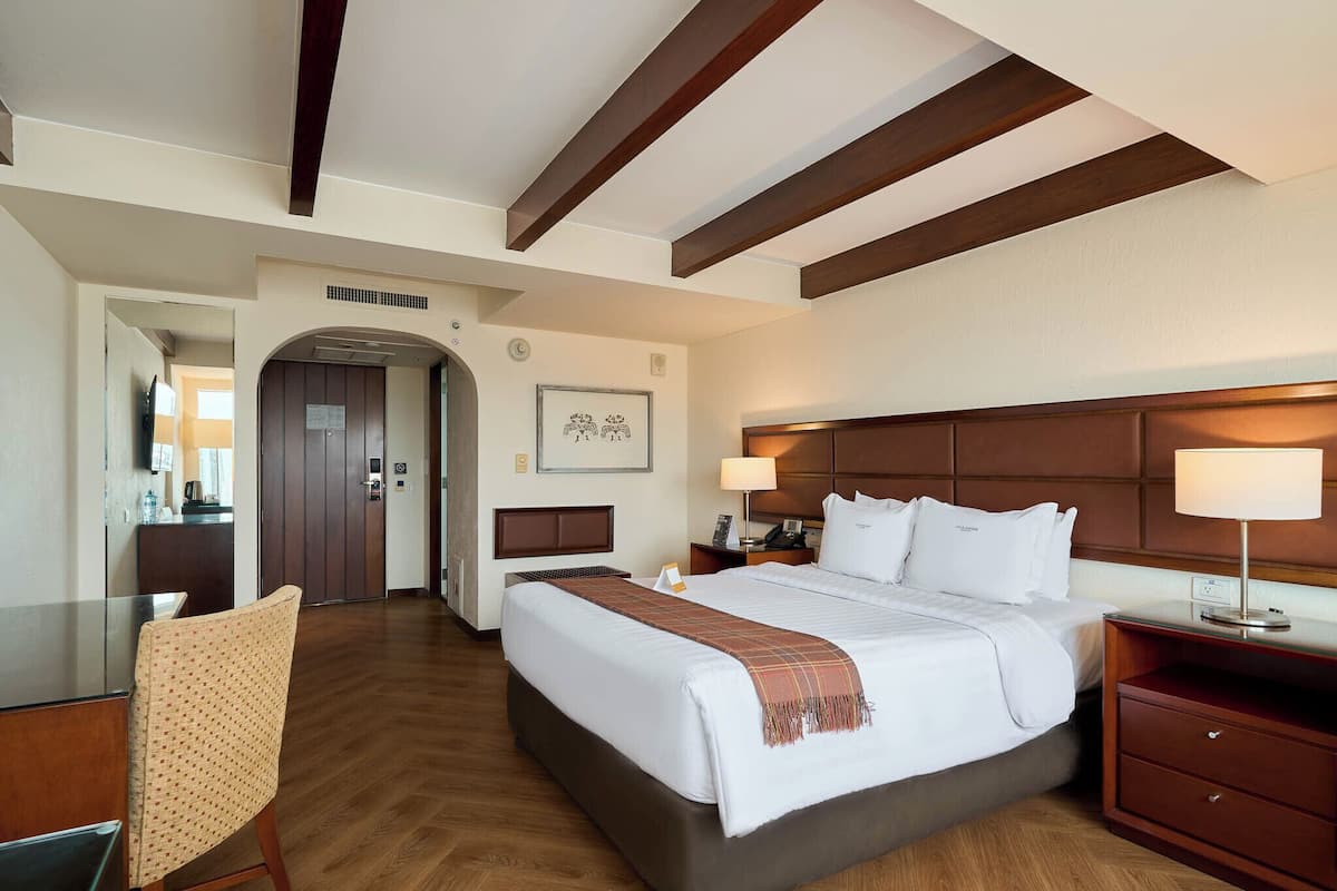 Une chambre d’hôtel avec un grand lit, un bureau, une chaise, un plafond en bois et une porte donnant sur une salle de bain.