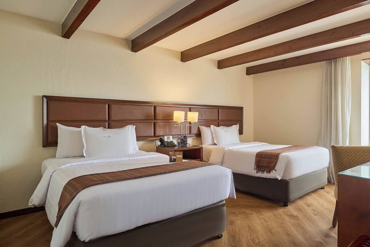 Une chambre d’hôtel avec deux lits, un plafond en bois, une table de chevet avec des lampes et une chaise.
