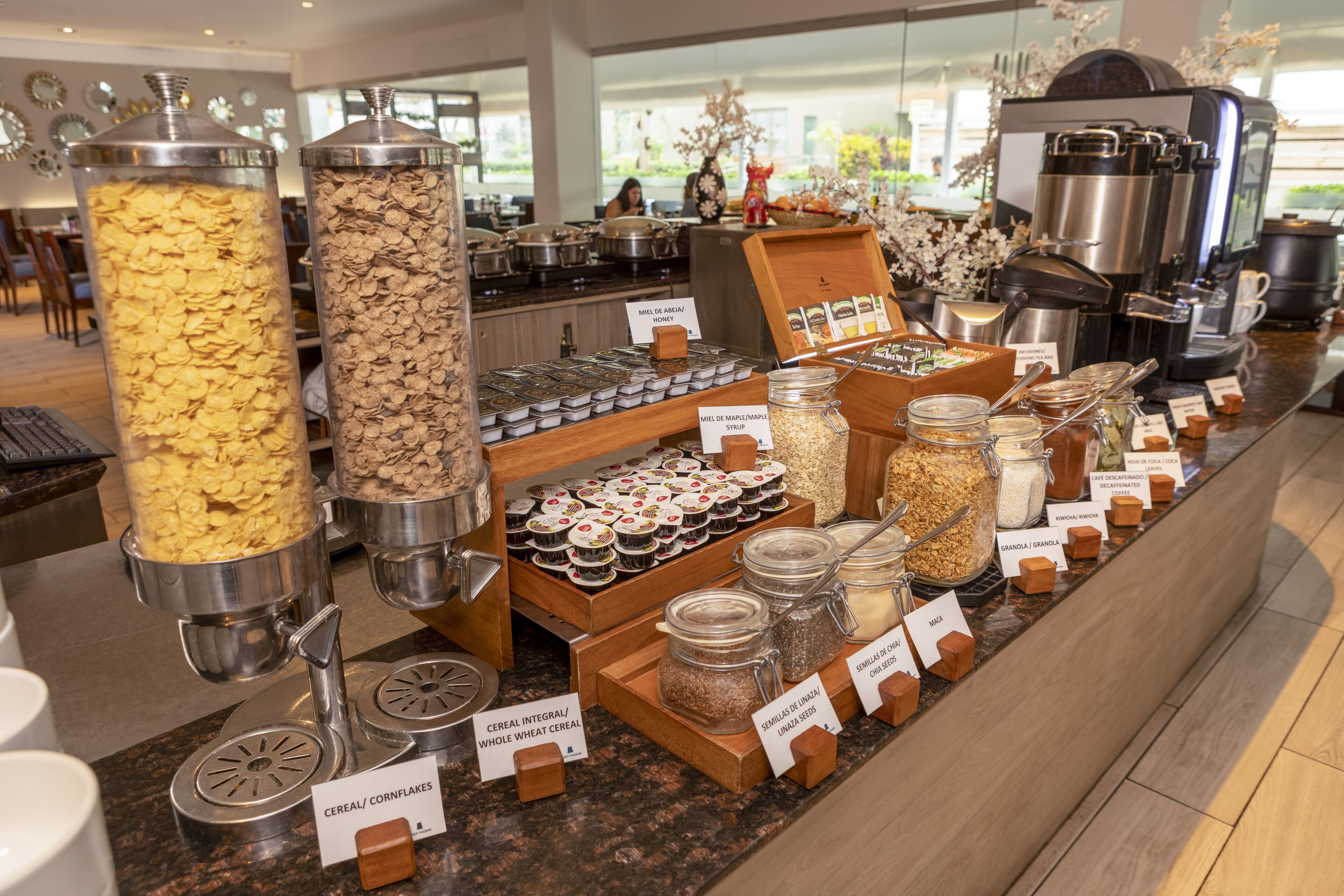 A breakfast buffet with various cereal options, coffee machines, and a coffee station.