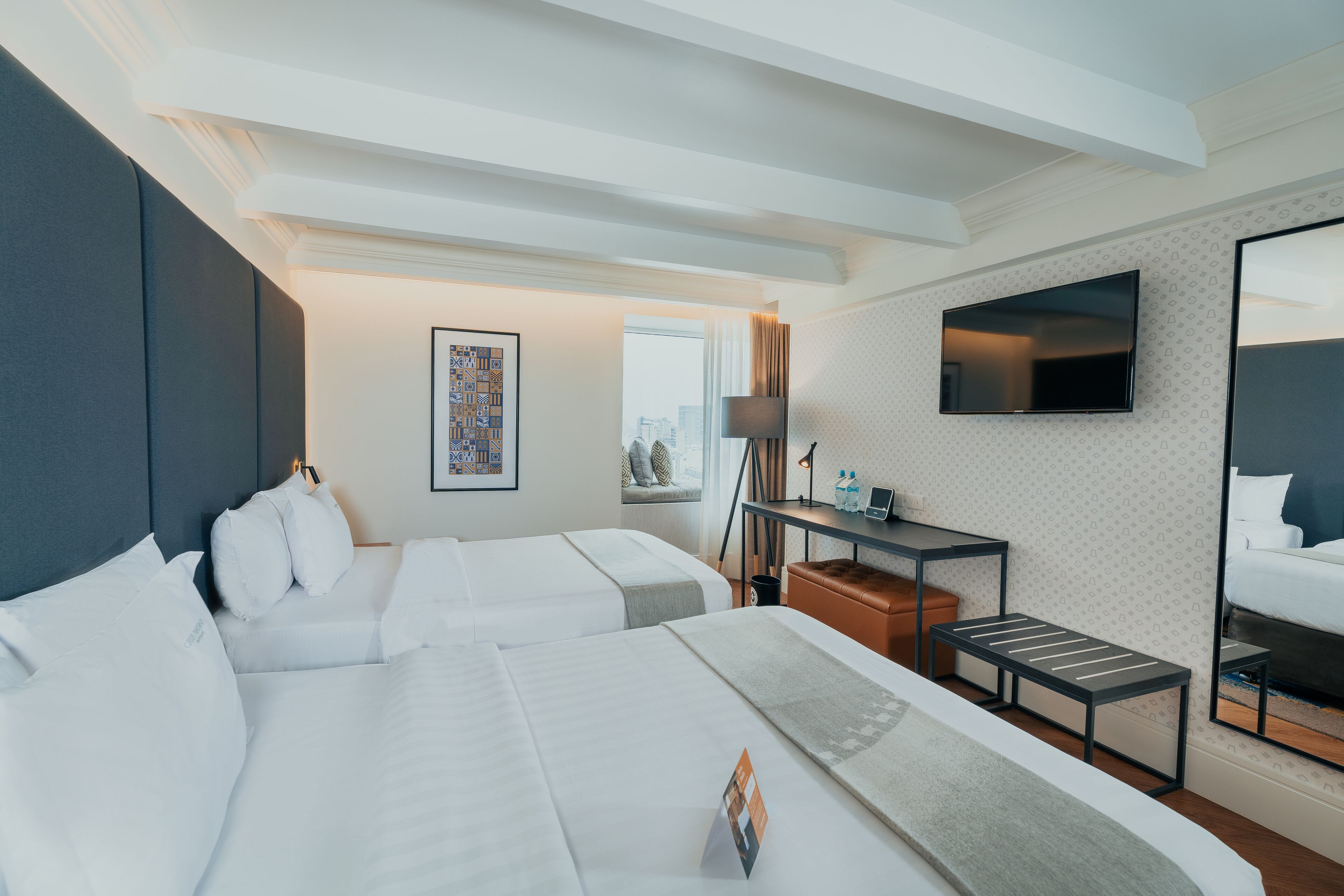 Habitación de hotel con dos camas, televisión, escritorio con lámpara y ventana con vista.