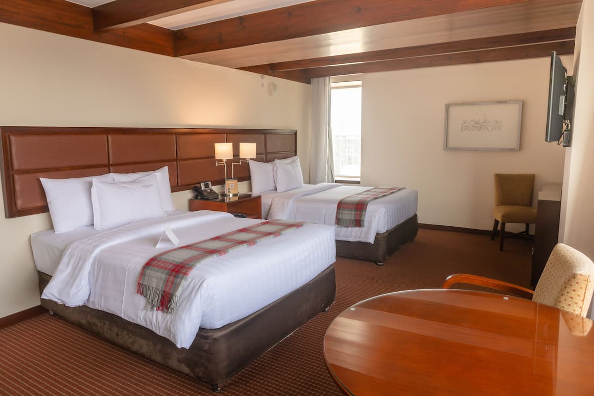 Une chambre d’hôtel avec deux lits, une tête de lit en bois, une table de chevet avec des lampes, une chaise et un téléviseur.