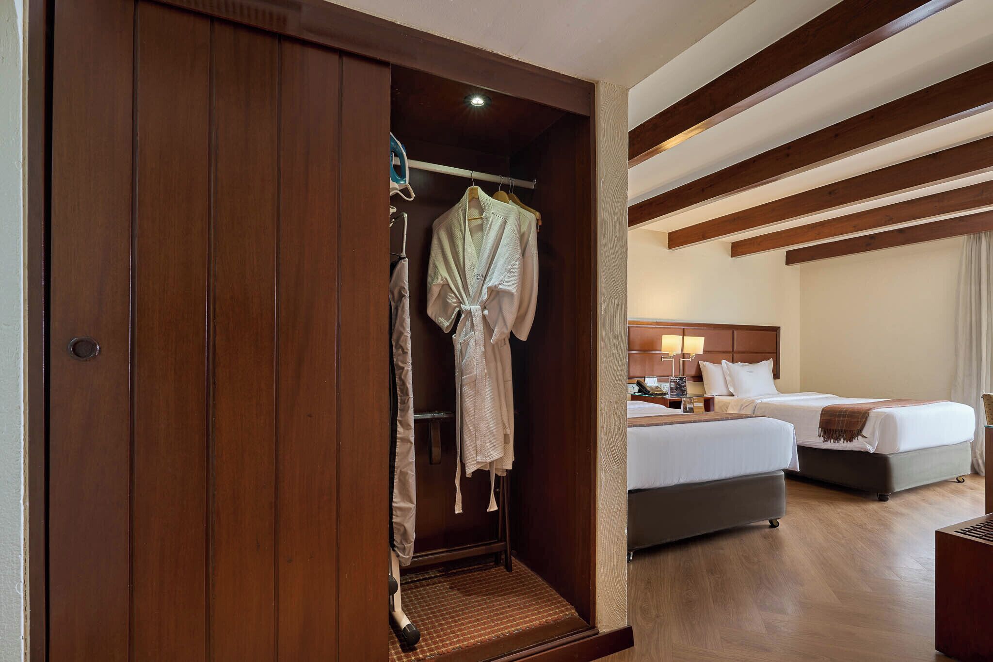 Una habitación de hotel con un armario de madera, una cama, una mesita de noche y una bata colgada.